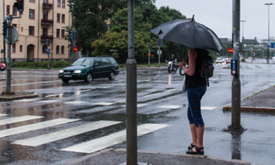 Kvinna med paraply väntar på att gå över gatan
